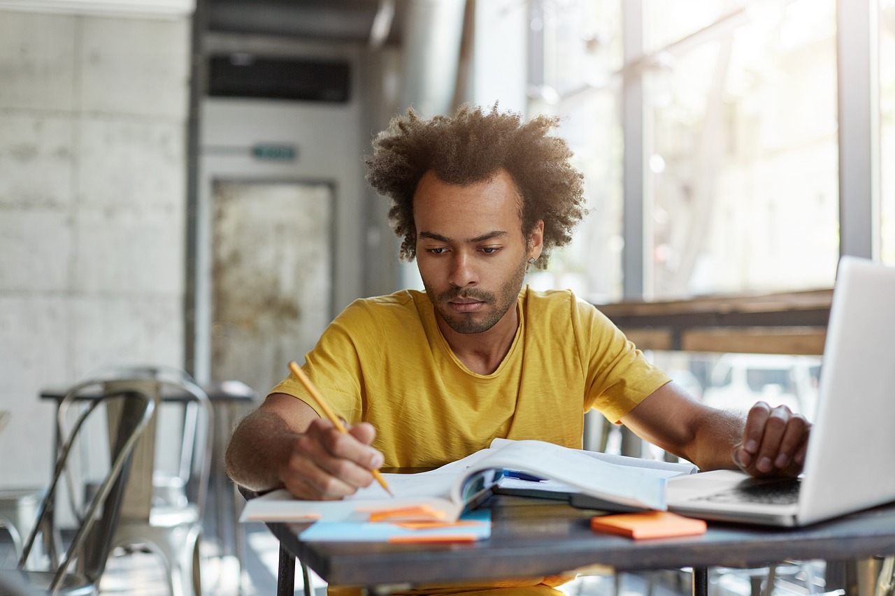 Image d'un jeune homme en train d'étudier un cours durant sa pause. Il consulte ses livres et son ordinateur.